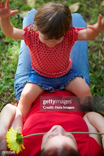 young woman lying on grass with her daughter sitting on her stomach - baby girl laying on tummy stock pictures, royalty-free photos & images