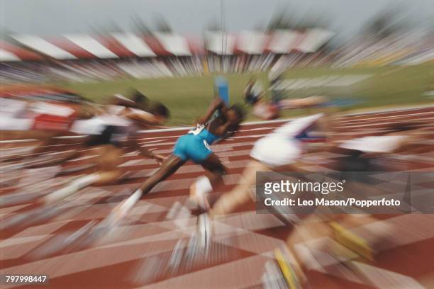 Zoom pull view of male sprinters accelerating from their starting blocks in the first seconds of a 100 metres race at an athletics track circa 1990.