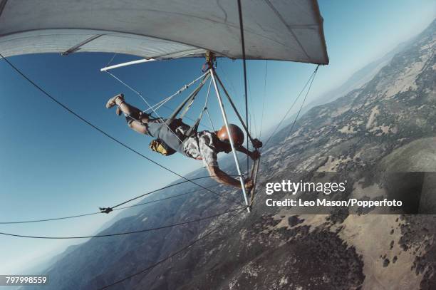 View of a pilot suspended under a hang glider as it flies over the Black Mountains range near Death Valley in California in 1981.