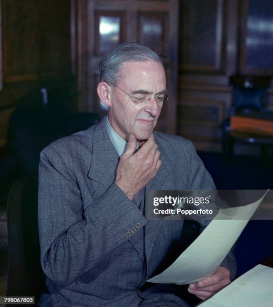 British Labour Party politician and recently appointed President of the Board of Trade, Stafford Cripps pictured reading documents at his office desk...