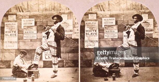 Stereoscopic image of an African American man as he gets a shoeshine from a young boy on the sidewalk. Anti-slavery posters hang on the wall behind...
