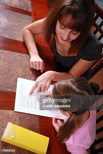 a mother (or tutor) pointing out an error on the little girl's math worksheet. - tuition assistance stock pictures, royalty-free photos & images