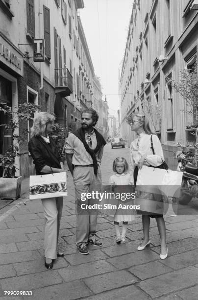 Italian fashion designer Gianni Versace with two women and a girl, on a street in Italy, circa 1980. The two shoppers are carrying Versace bags.