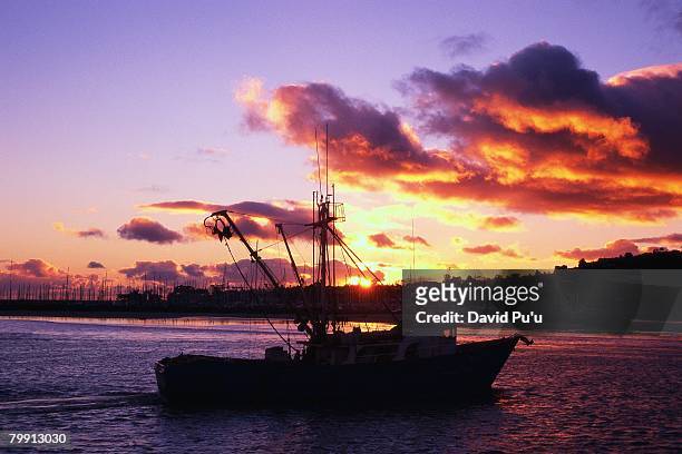 fishing vessel silhouetted at sunset - david puu stock-fotos und bilder