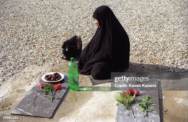 Woman sits at the grave of her son after having cleansed it with rosewater in Behesht-e Zahra cemetery, Tehran, where thousands of those killed in...