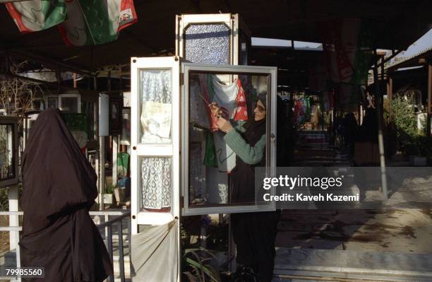 Woman tidies up a display case at her son's grave in Behesht-e Zahra cemetery, Tehran, where thousands of those killed in the Iranian Revolution and...