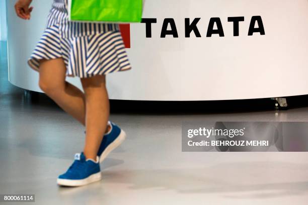 Woman walks past a logo of the Japanese auto parts maker Takata at a car showroom in Tokyo on June 23, 2017. - Takata shares swung wildly rebounding...