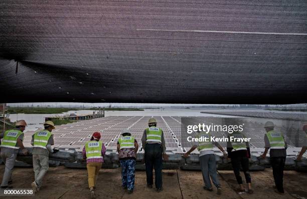 Chinese workers push a section of panels into the water that are part of a large floating solar farm project under construction by the Sungrow Power...