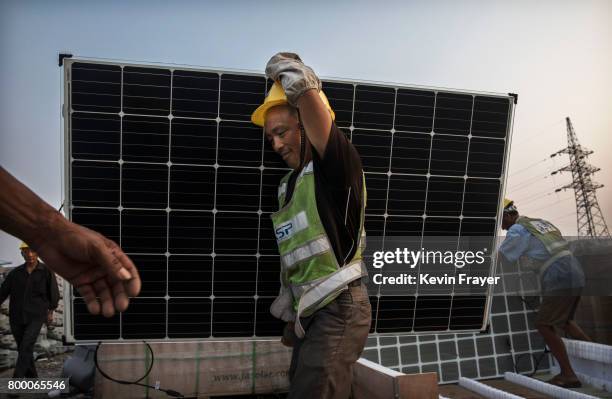 Chinese worker carries a panel that will be part of a large floating solar farm project under construction by the Sungrow Power Supply Company on a...