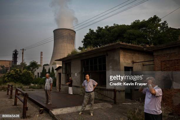 Chinese men exercise under a cooling tower at a coal fired power plant near the site of a large floating solar farm project under construction by the...
