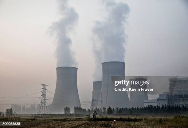 Chinese farmer works his field next to a state owned coal fired power plant near the site of a large floating solar farm project under construction...