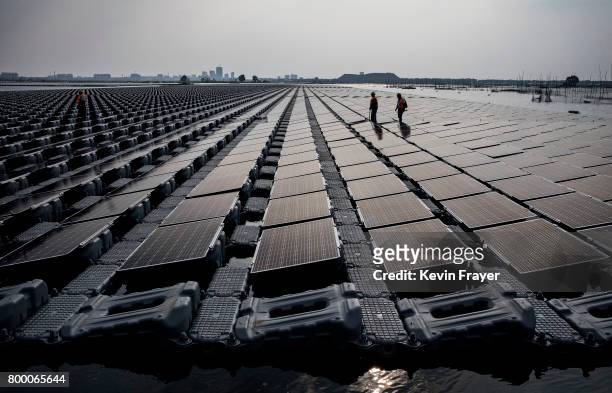 Chinese workers walk on a section of a large floating solar farm project under construction by the Sungrow Power Supply Company on a lake caused by a...