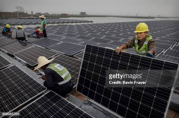 Chinese workers prepare panels that will be part of a large floating solar farm project under construction by the Sungrow Power Supply Company on a...
