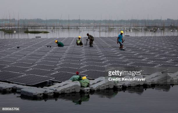 Chinese workers walk on a section of a large floating solar farm project under construction by the Sungrow Power Supply Company on a lake caused by a...