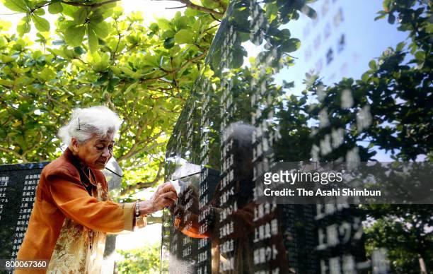 Woman cleans with a cloth the names of her mother and other relatives engraved on the Cornerstone of Peace at the Peace Memorial Park on the 72nd...