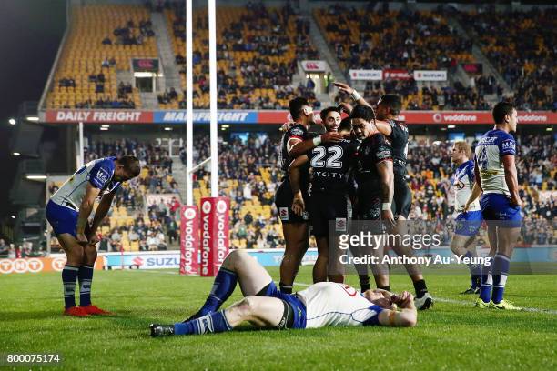 Ken Maumalo of the Warriors celebrates with teammates after scoring a try as James Graham of the Bulldogs takes a breather on the ground during the...