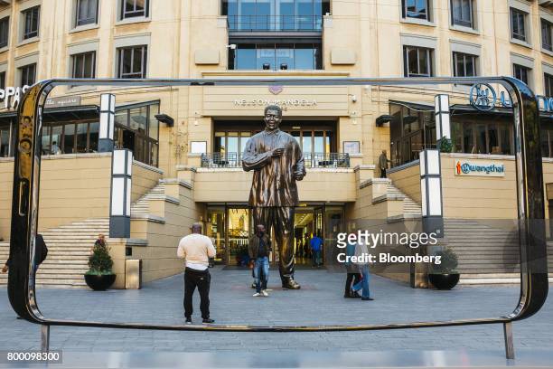 Pedestrians pass a statue of Nelson Mandela, former South African president, seen through a giant mobile phone frame in Nelson Mandela Square in the...