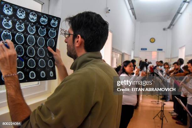 Doctor looks at a cat-scan as volunteer members of Musica Para el Alma perform for patients at the Alvarez Hospital in Buenos Aires on June 12, 2017....