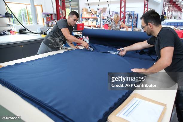 Employees cut a piece of textiles, at the sewing studio of the production plant of the French sport clothing and equipment brand Le Coq Sportif, in...