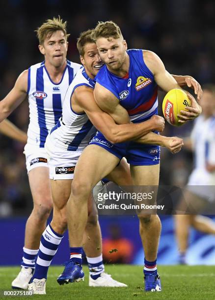 Jake Stringer of the Bulldogs handballs whilst being tackled by Andrew Swallow of the Kangaroos during the round 14 AFL match between the Western...