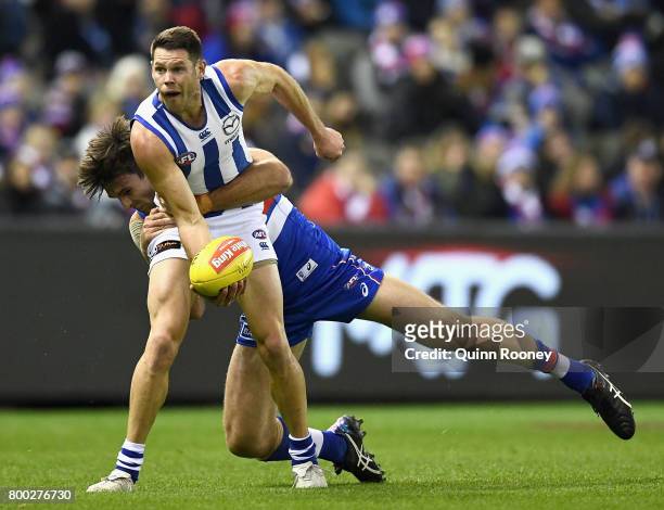 Sam Gibson of the Kangaroos handballs whilst being tackled Tom Campbell of the Bulldogs during the round 14 AFL match between the Western Bulldogs...