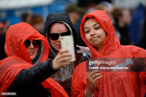 Festival goer taking a selfie with a smartphone while walking through rain and mud at the camp site of the Hurricane Festival 2017 after a night full...