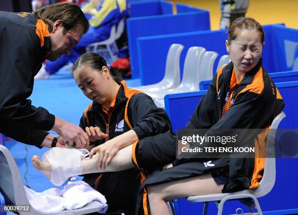 Li Jie of the Netherlands reacts as a Dutch trainer and player Li Jiao attend to her injured foot during Li's quarter-final match against Singapore...