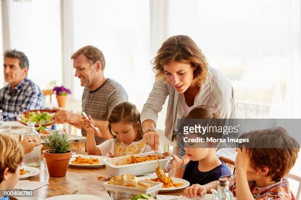 mother serving food to children against window - pranzo foto e immagini stock