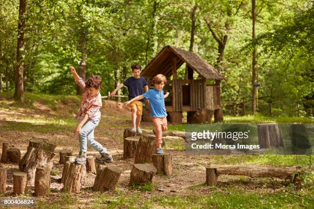 friends playing on tree stumps in forest - divertirsi foto e immagini stock