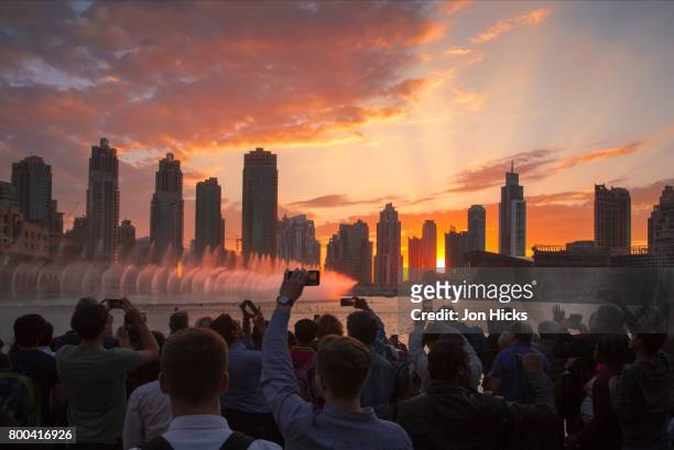 crowds watch the dubai fountain show at sunset in burj khalifa lake. - dubai tourism stock pictures, royalty-free photos & images