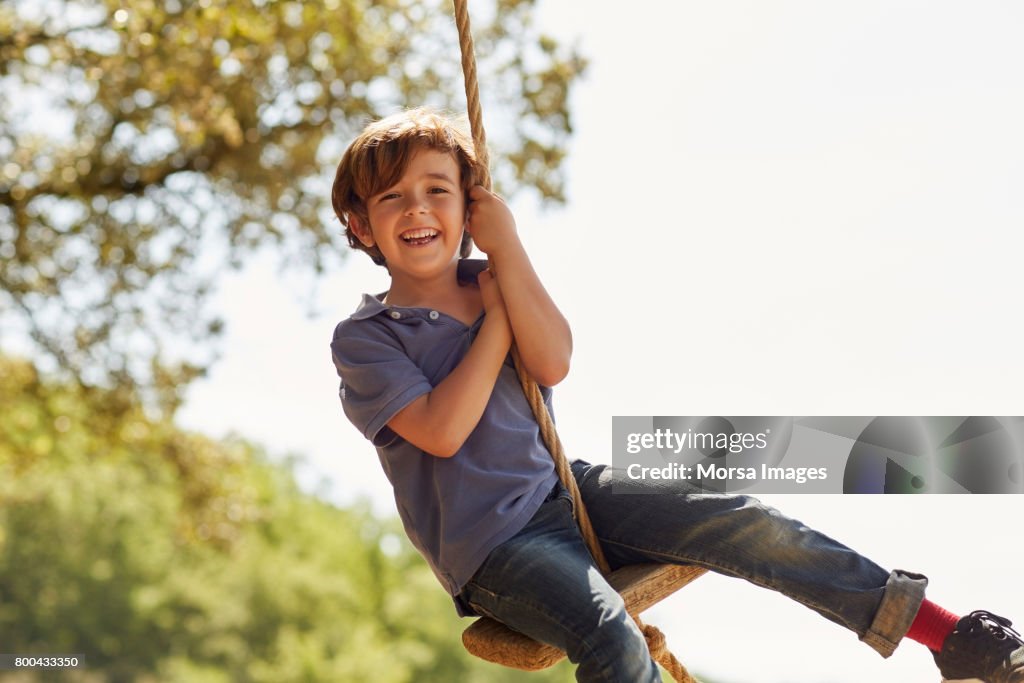 Retrato de niño feliz jugando en columpio contra cielo