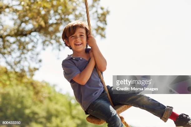 portrait de l’heureux garçon jouant sur balançoire contre ciel - joue photos et images de collection