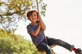 Portrait of happy boy playing on swing against sky