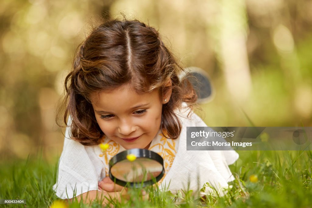 Girl looking at grass through magnifying glass