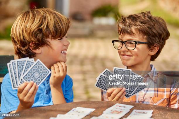 smiling brothers playing cards at table in yard - child play table stock pictures, royalty-free photos & images