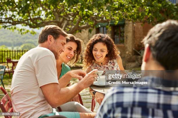 man showing mobile phone to female friends in yard - tea outdoor stock pictures, royalty-free photos & images