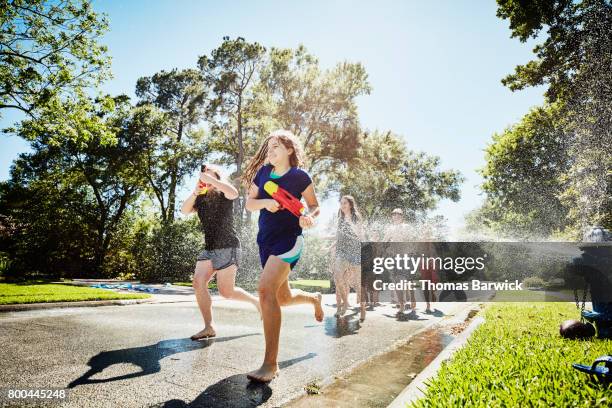 smiling teen friends with squirt guns running through spray from fire hydrant on summer afternoon - teen boy shorts stockfoto's en -beelden