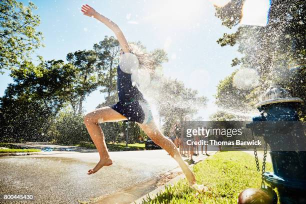 teen girl running through spray from fire hydrant on summer afternoon - hydrant stock-fotos und bilder