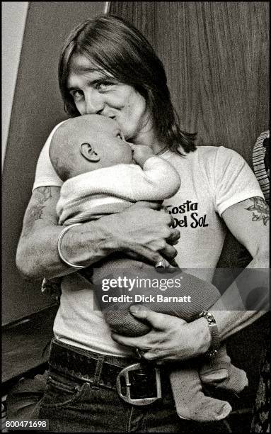 Phil Rudd of AC/DC holding a baby at a WEA Records press event, London, 1976.