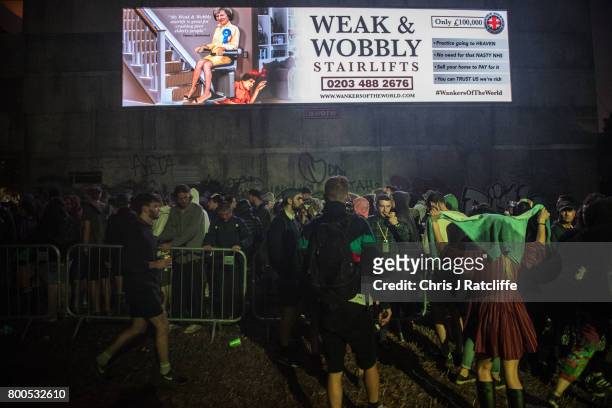 Revellers queue underneath a politcal sign about Theresa May to enter a club in Block 9 in the Shangri La area at Glastonbury Festival Site on June...