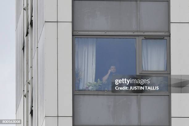 Man uses a mobile phone as he looks out of a window from a flat in Dorney Tower residential block on the Chalcots Estate in north London on June 24,...