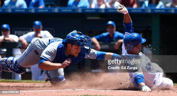 Alcides Escobar of the Kansas City Royals slides safely into home to score past the tag of Luke Maile of the Toronto Blue Jays in the third inning at...