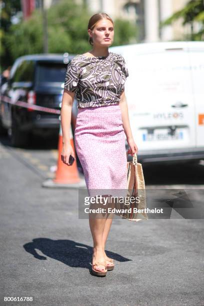 Guest wears a pink skirt, a t-shirt with prints, a straw bag, and sandals, outside the Dior show, during Paris Fashion Week - Menswear Spring/Summer...
