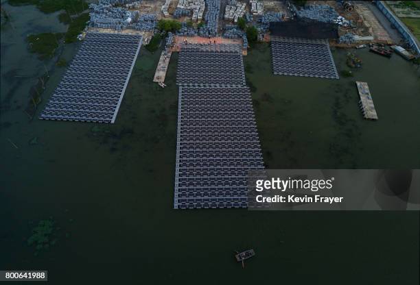 Chinese fisherman paddles passed workers building a large floating solar farm project under construction by the Sungrow Power Supply Company on a...