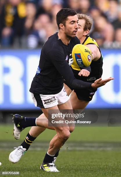 Kade Simpson of the Blues handballs whilst being tackled by David Astbury of the Tigers during the round 14 AFL match between the Richmond Tigers and...