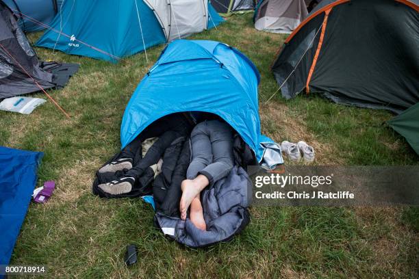 Two men sleep in a very small tent with their legs out stretching out of the door in a campsite at Glastonbury Festival Site on June 25, 2017 in...