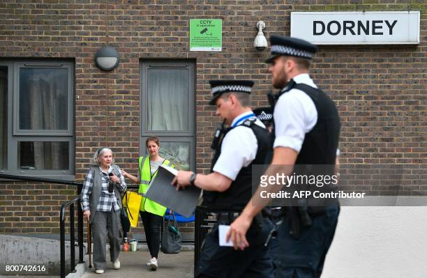 Council worker helps a resident leave Dorney Tower residential block on the Chalcots Estate in north London on June 25, 2017 as police are seen...