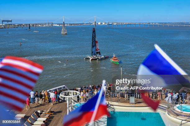 Picture taken from the cruise liner RMS Queen Mary 2 shows passengers waving the French and US flags, as French skipper Francois Gabart sails his...