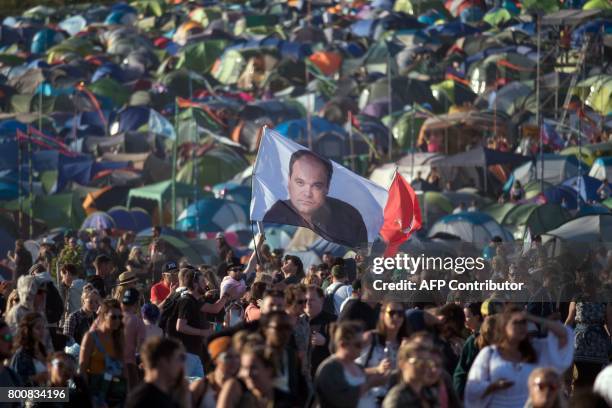 Festival-goer carries a flag bearing the image of actor Shaun Williamson, who is best known for playing the character Barry Evans in the soap opera...