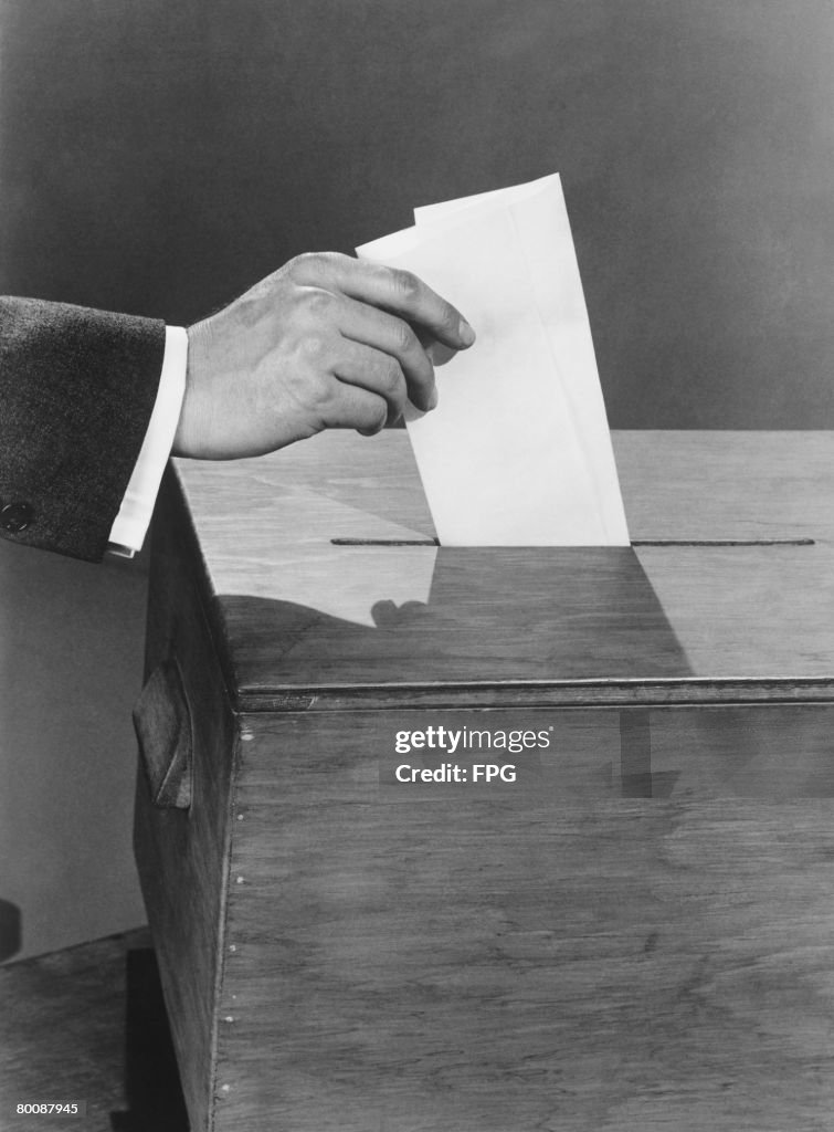 Man putting ballots into box, close up of hand